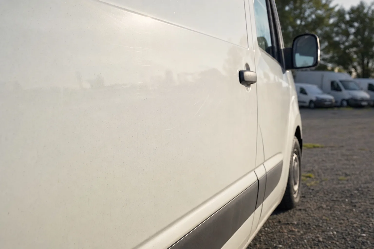 Flanc d'un utilitaire blanc en lumière rasante révélant de légères éraflures